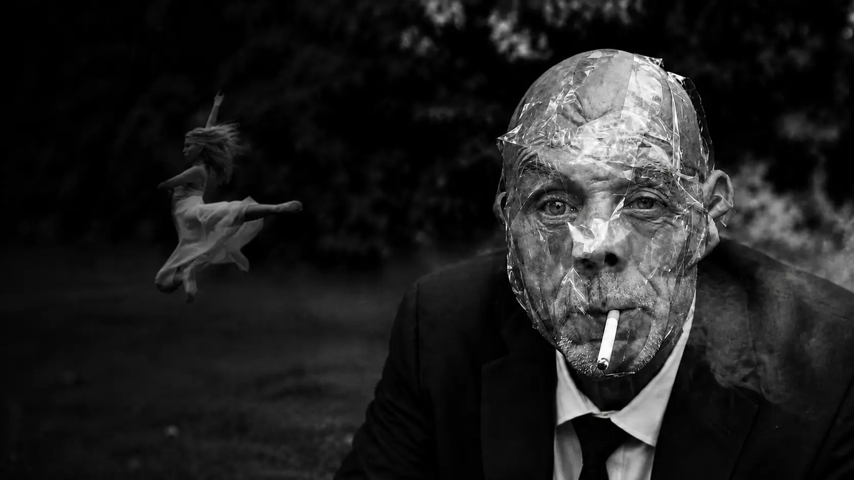 Un homme au visage recouvert de ruban adhésif, cigarette aux lèvres, devant une danseuse suspendue dans les airs — photographie de Frédéric Vignale